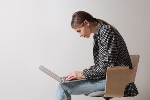 Frau sitzt mit Buckel an Laptop und sollte ihre schlechte Körperhaltung verbessern